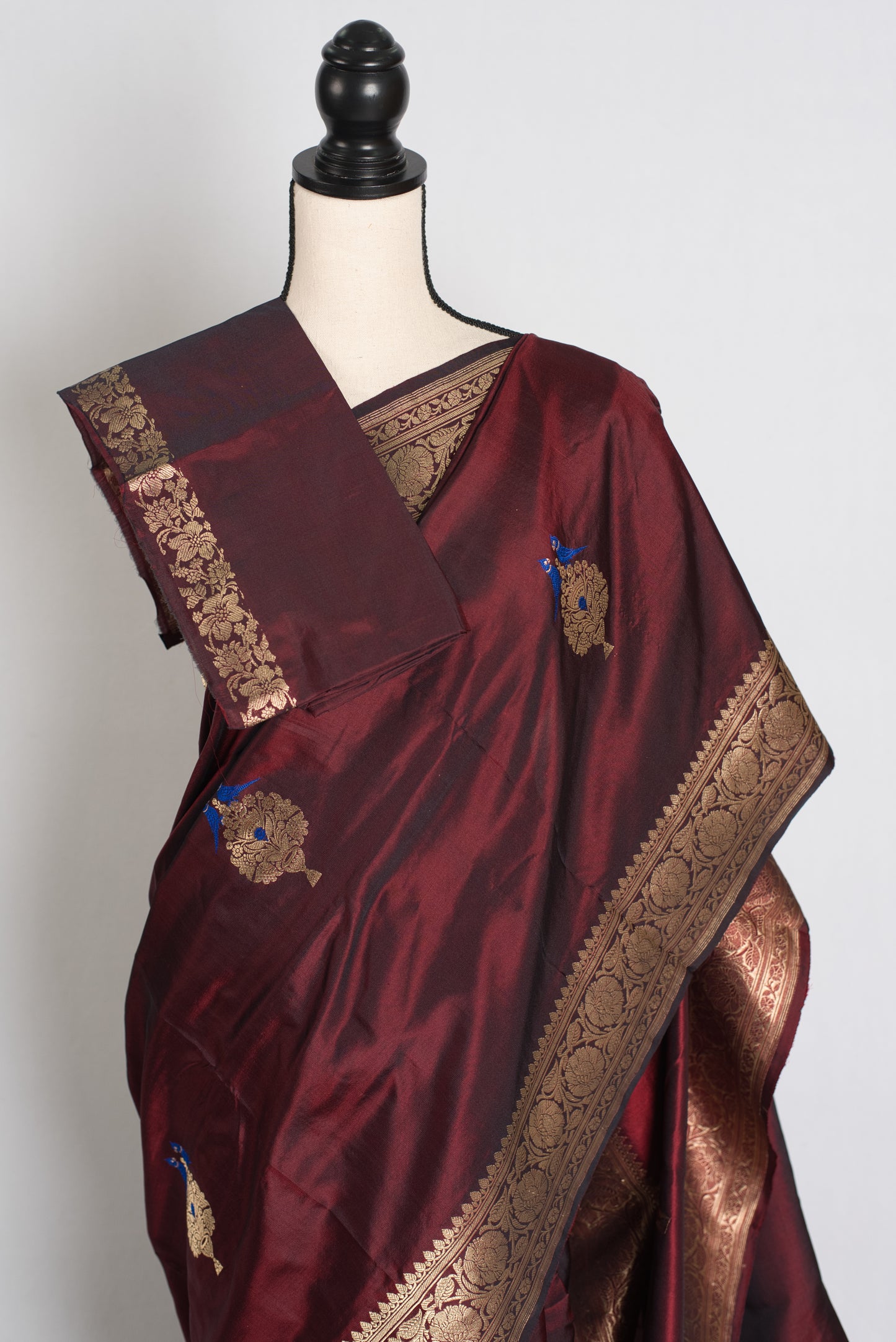 Maroon saree with gold embroidery on a mannequin against a white background