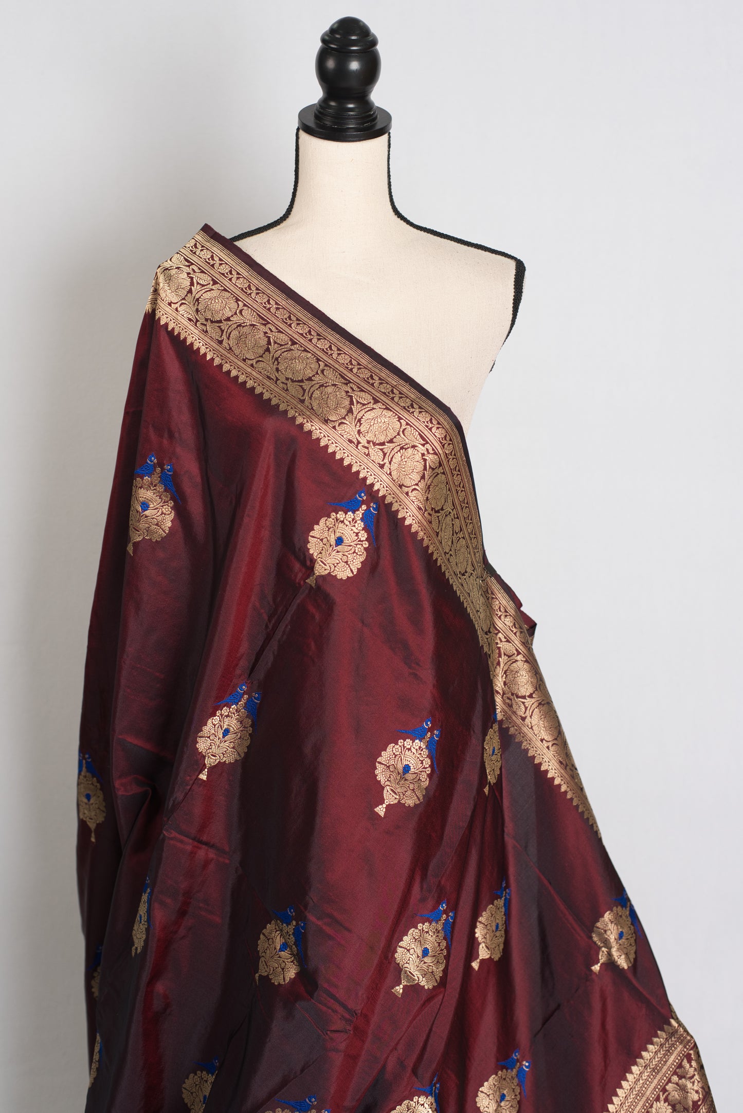Maroon saree with gold and blue embroidery on a mannequin against a white background