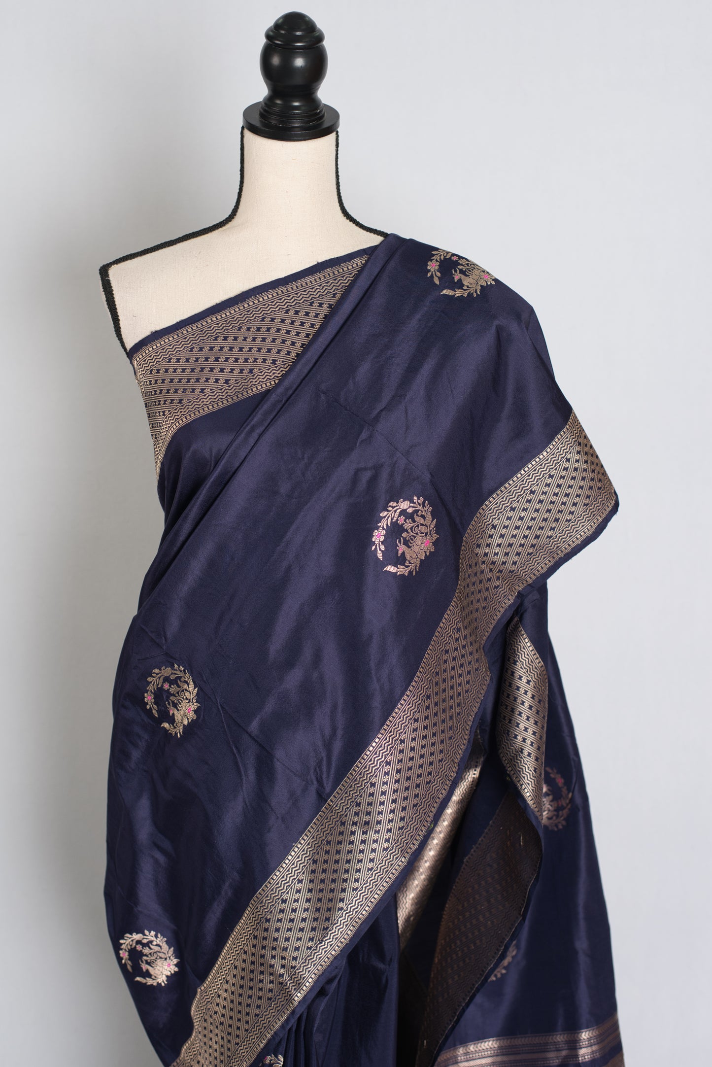 Navy blue saree with gold embroidery on a mannequin against a white background