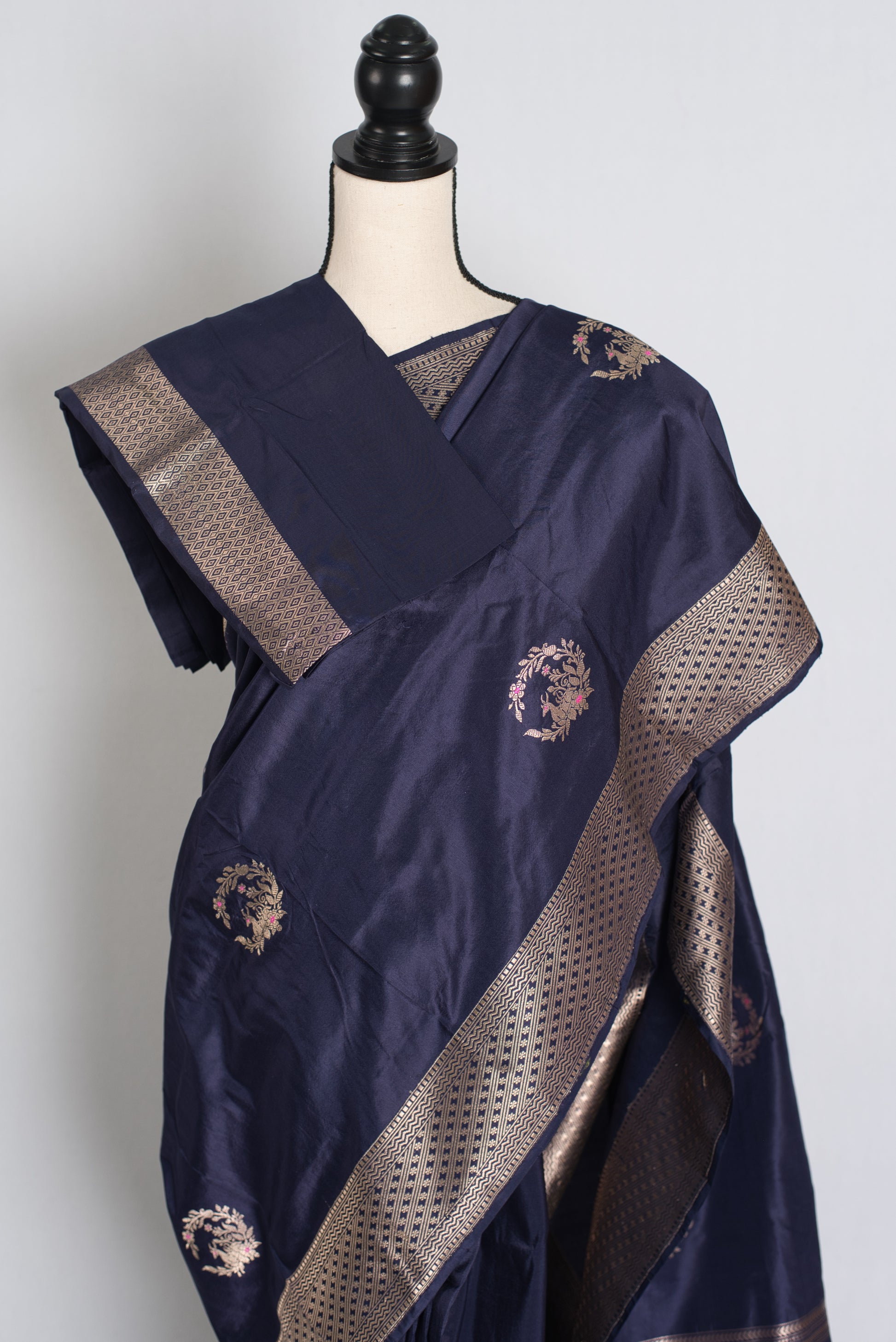 Navy blue saree with gold embroidery on a mannequin against a white background