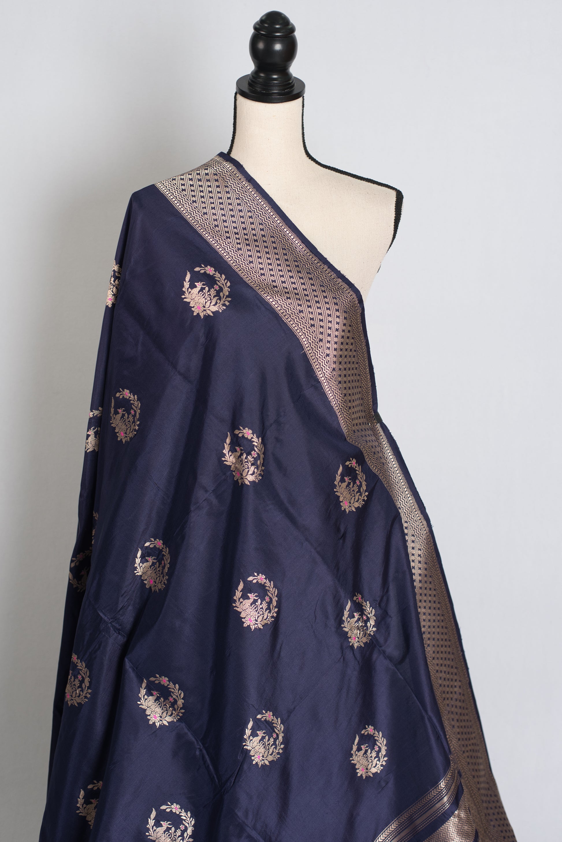 Navy blue saree with gold embroidery on a mannequin against a white background