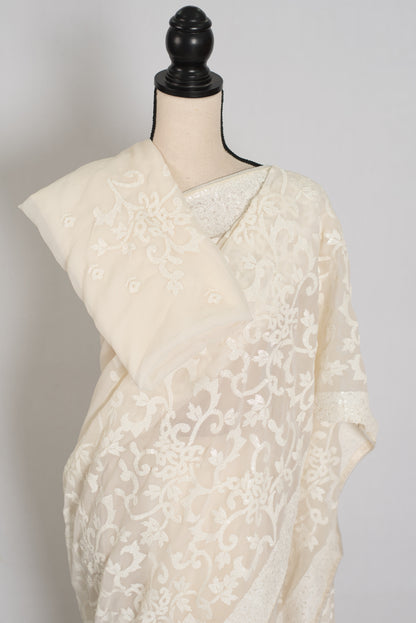 An off-white/cream sheer embroidered saree draped on a cream-colored dress form mannequin, set against a plain light gray background.