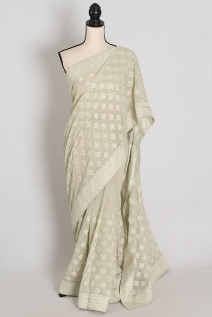 A light sage green saree with a white geometric pattern and a wide border, displayed on a mannequin against a plain light gray background.